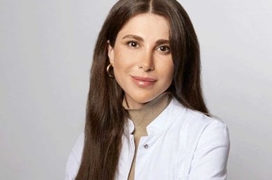 Portrait von Dr. Emi Arpa Dermatologin in weißem Kittel vor neutralem Hintergrund