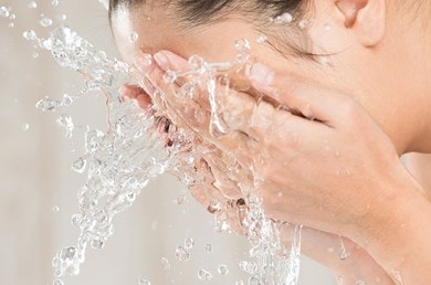 Frau wäscht sich das Gesicht mit klarem Wasser
