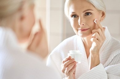 Ältere Frau trägt im Spiegel Gesichtscreme zur Anti-Aging-Pflege auf