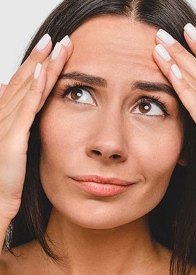 Eine Frau mit besorgtem Blick streicht mit den Fingern beider Hände über ihre Stirnfalten