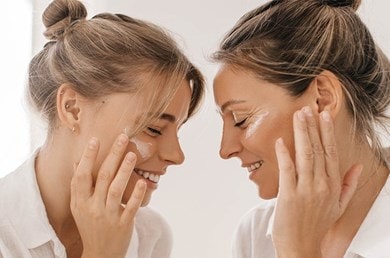 Zwei Frauen, die sich mit geschlossenen Augen gegenüberstehen, und jeweils Augencreme auftragen